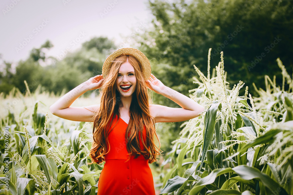 red-haired girl with freckles in red dress walking on a field of corn ...