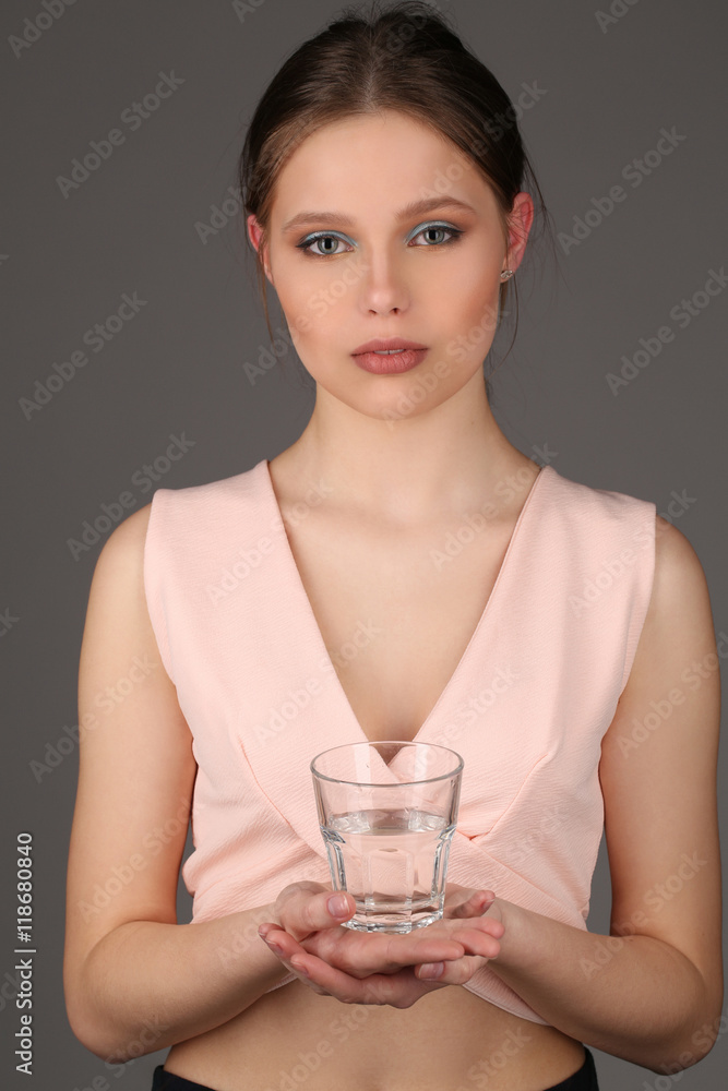 Model in pink top holding glass of water. Close up. Gray background Model in pink top holding glass of water. Close up. Gray background