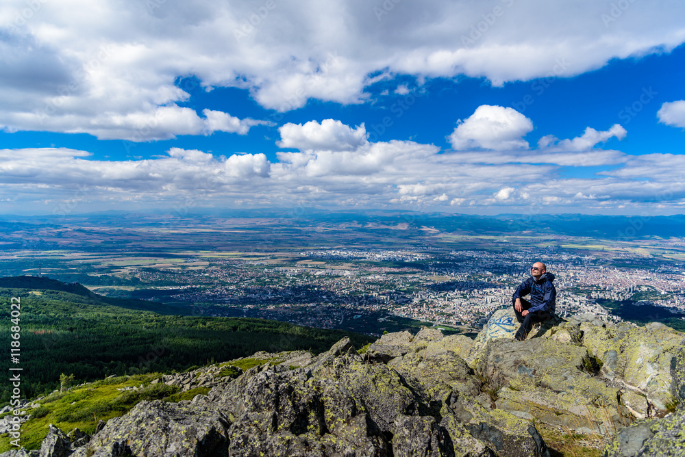 Middle aged man on top of Vitosha mountain, Sofia, Bulgaria - looking towards the sun, with sun glasses - city in the far background