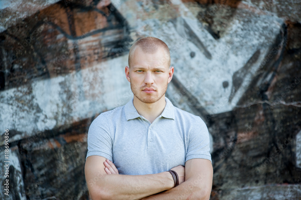 Portrait of the young man against the background of a concrete wall with graffiti. The guy looks at the camera. Portrait of the young man against the background of a concrete wall with graffiti. The guy looks at the camera.