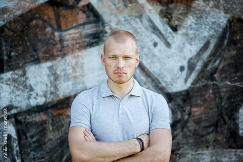 Portrait of the young man against the background of a concrete wall with graffiti. The guy looks at the camera.