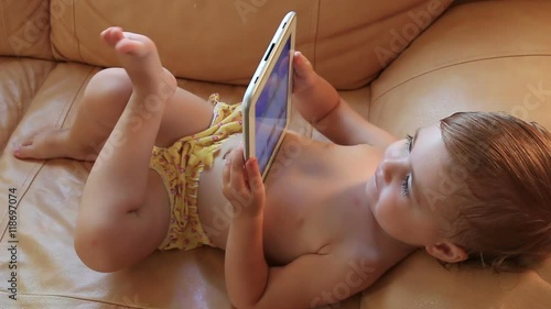 little baby lying on the couch playing with the tablet. Full HD. 1920x1080