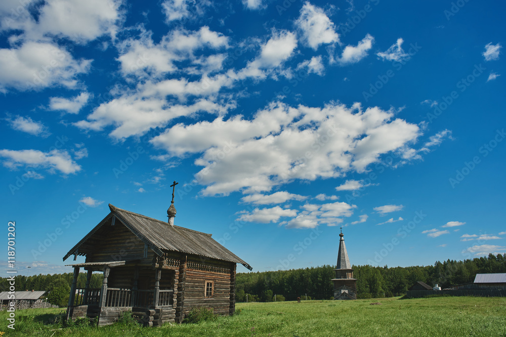 wooden house church with a cross on the roof on a green glade in a forest under a blue sky with clouds