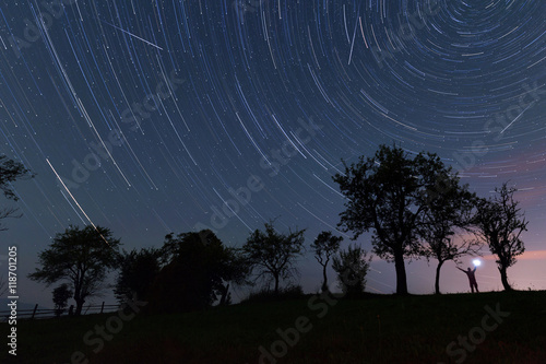 Trees and man silhouette over star tracks
