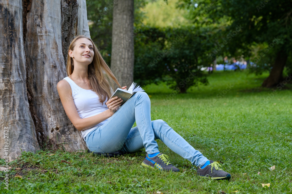 Young woman reading a book in the park and dreaming Young woman reading a book in the park and dreaming