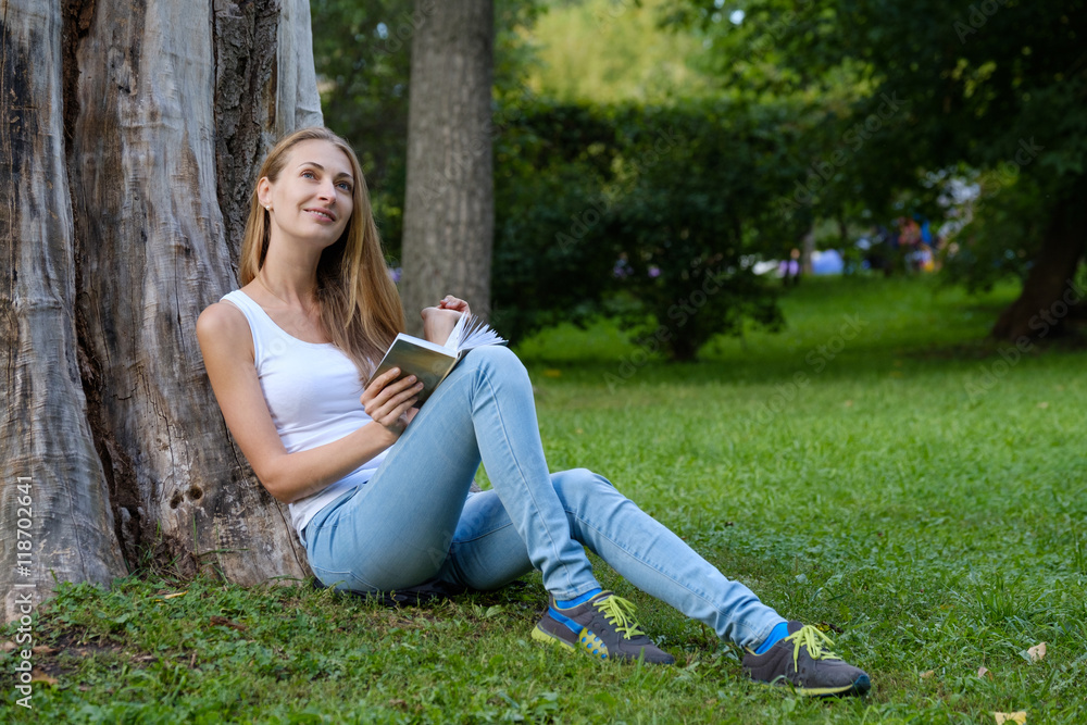 Young woman reading a book in the park and dreaming Young woman reading a book in the park and dreaming
