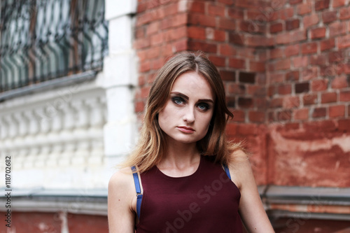 Young pretty woman portrait. Outdoor portrait of a young cute blond woman with a long hair. Model stands. Old brick wall background. Beautiful face eyes and lips.