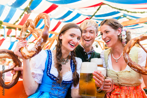 Drei Freunde auf der Dult oder Oktoberfest beißen in Riesenbrezen und trinken Bier im Bierzelt