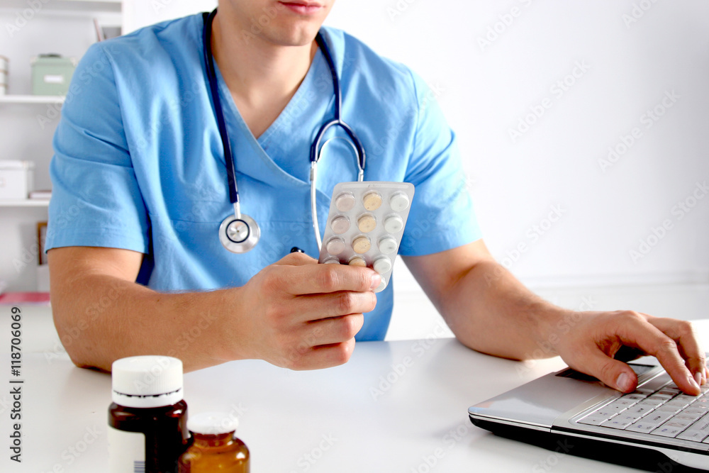 Male doctor sitting at the table and holding bottle Male doctor sitting at the table and holding bottle