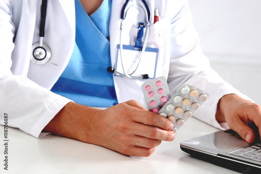 Male doctor sitting at the table and holding bottle Male doctor sitting at the table and holding bottle