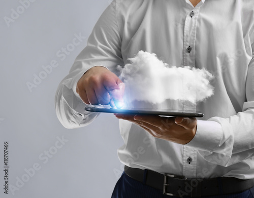 Businessman using tablet on gray background. Cloud computing and information storage concept.
