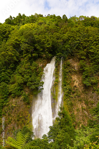 Scenic waterfall near Furnas in Azores, Portugal. Rain forest on a hill and waterfall in sight near a road from Furnas to Ribeira Quente on Sao Miguel Island.