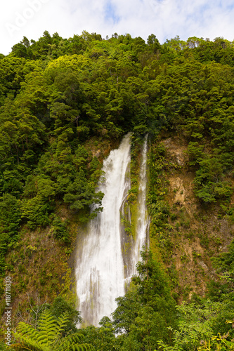 Scenic waterfall near Furnas in Azores  Portugal. Rain forest on a hill and waterfall in sight near a road from Furnas to Ribeira Quente on Sao Miguel Island.