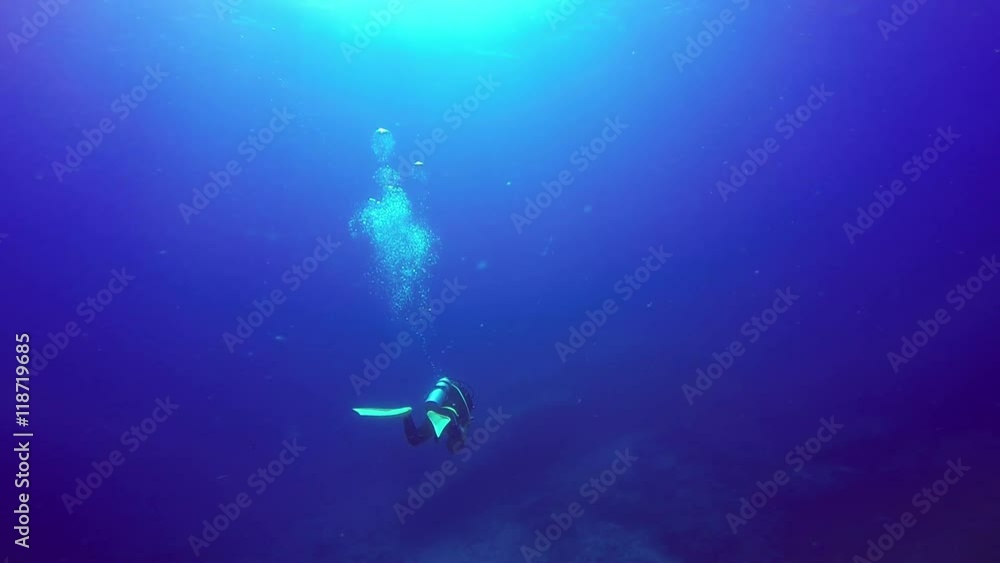 Underwater shoot of a scuba divers swimming in a blue clear water.