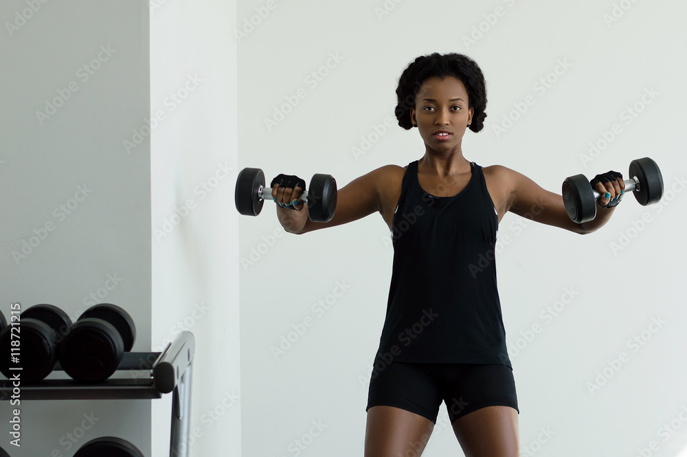 African woman in black t-shirt and shorts doing exercises in a gym