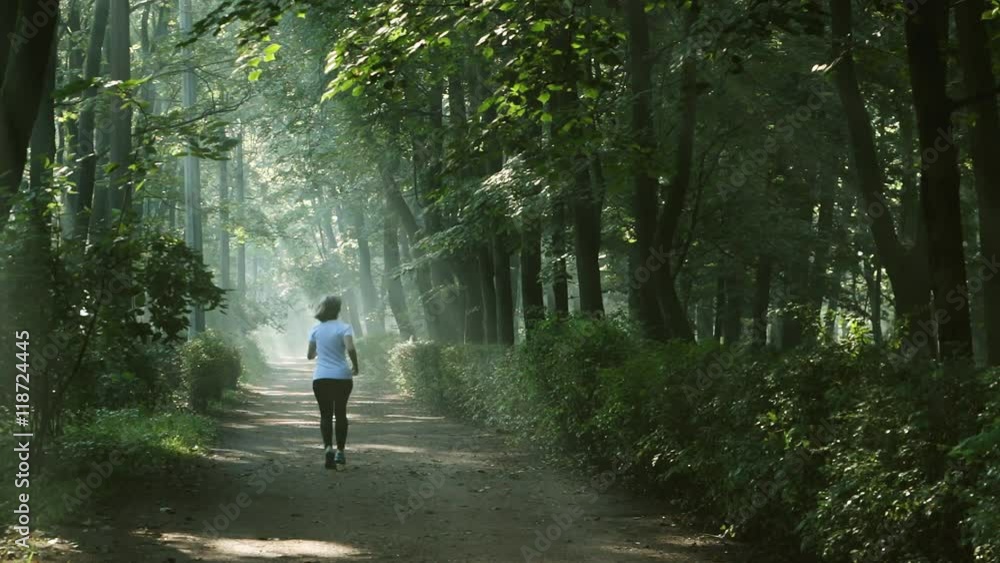 Woman running in the morning along walkway in the park in the slanting rays of the rising sun. Woman running in the morning along walkway in the park in the slanting rays of the rising sun.