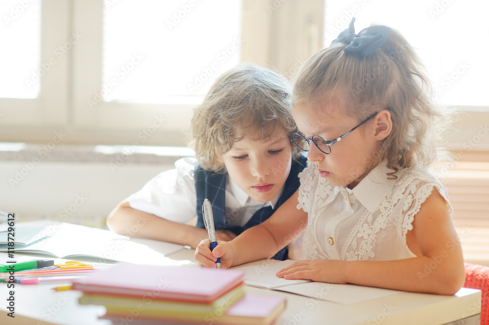 Two little classmate, boy and girl, are sitting at the same desk Two little classmate, boy and girl, are sitting at the same desk