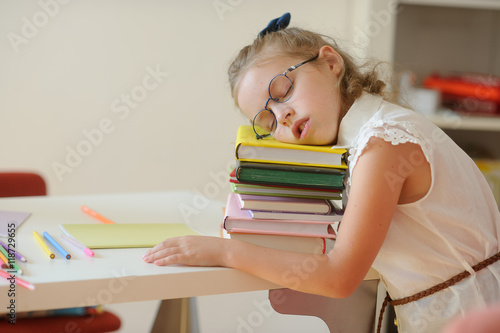 Little schoolgirl fall asleep on a pile of books.