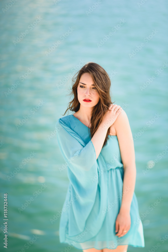 Woman with blue eyes wearing blue dress in the beach.