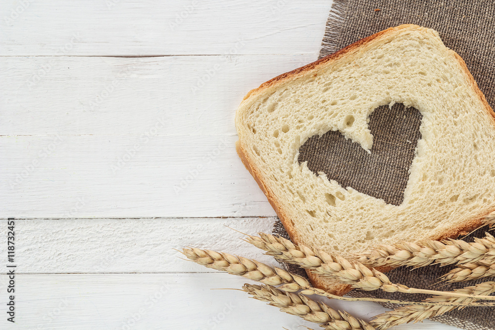 Slice of white bread with a heart carved in them and wheat ears