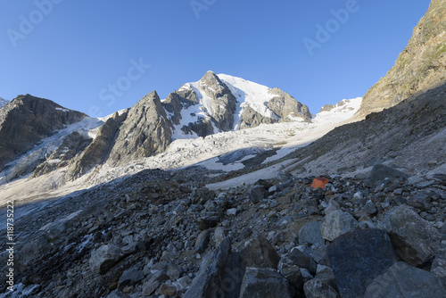Orange tent among stones in highland camp against mountains and