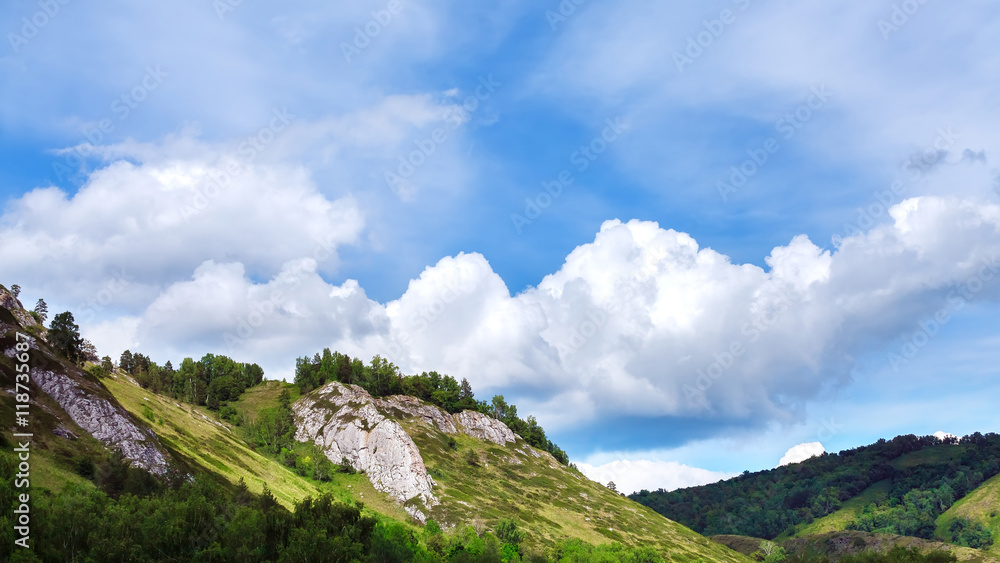 Mountain range with trees and vegetation under blue sky and clouds. (Russia)