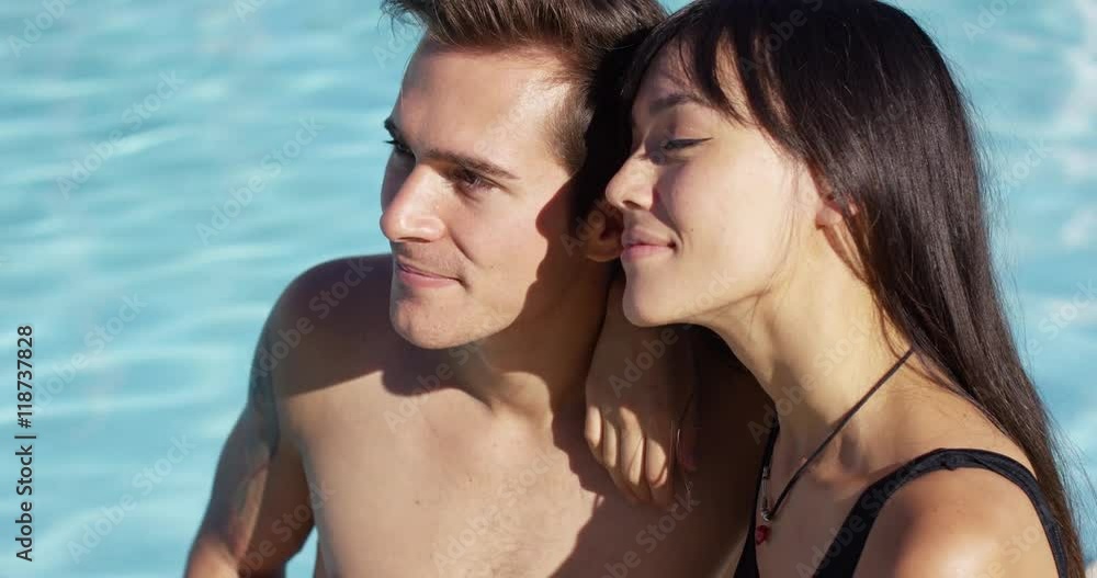 Sunbathing couple sit beside swimming pool and enjoy the sun gently falls on their skin Sunbathing couple sit beside swimming pool and enjoy the sun gently falls on their skin