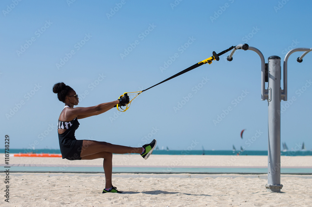 Young woman of african ethnicity balancing using special ropes for suspension training. Outdoor sport activity concept - obrazy, fototapety, plakaty 