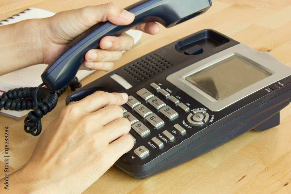 Female Hand Holding Phone Receiver And Dialing Number In Workplace Female Hand Holding Phone Receiver And Dialing Number In Workplace