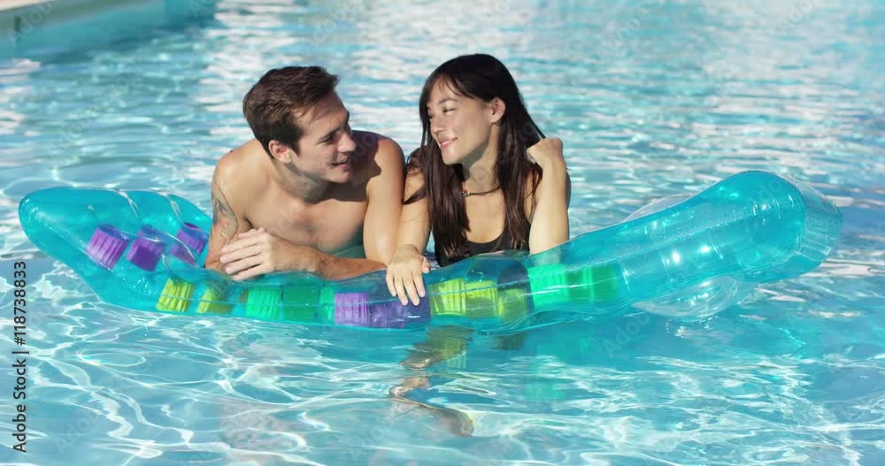 Pair of attractive male and female adults floating together on inflatable floating plastic mattress in outdoor pool Pair of attractive male and female adults floating together on inflatable floating plastic mattress in outdoor pool