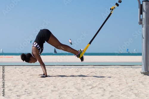 Young african woman performing difficult exercise using ropes for suspension training at Dubai beach in UAE