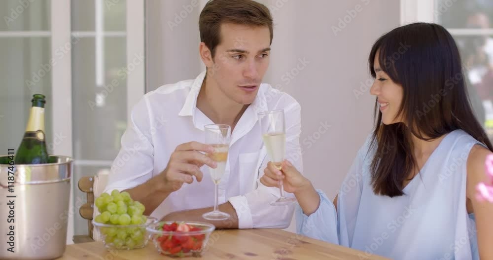 Cheerful grinning adult couple toasting champagne glasses in celebration of something at table with fruit bowls Cheerful grinning adult couple toasting champagne glasses in celebration of something at table with fruit bowls