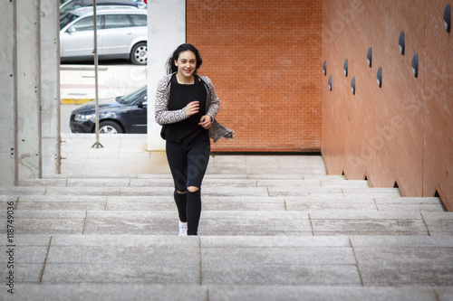 Chica joven morena subiendo y bajando feliz las escaleras en la ciudad. Modelo morena posando en las escaleras.