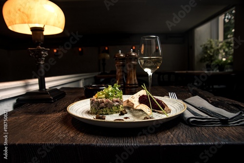 Salmon tartare with a glass of wine on a white plate in a restaurant, side view. Photo for the menu