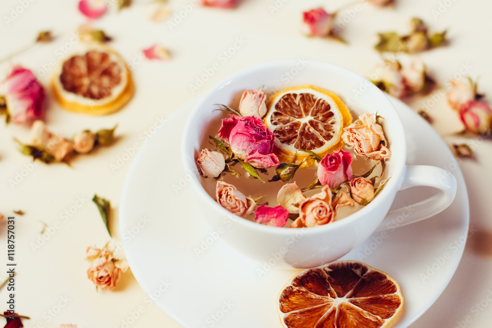 Herbal tea in white Cup and saucer with roses and dried flowers dried round slices of lemon laid on a white background - obrazy, fototapety, plakaty 