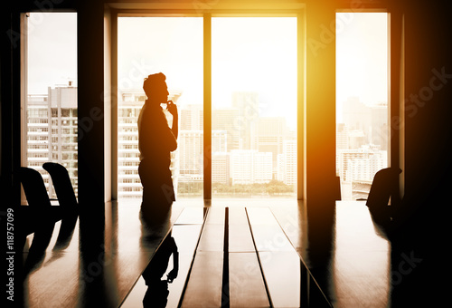 Silhouette of businessman thinking in meeting room with cityscape in background in evening sunlight.