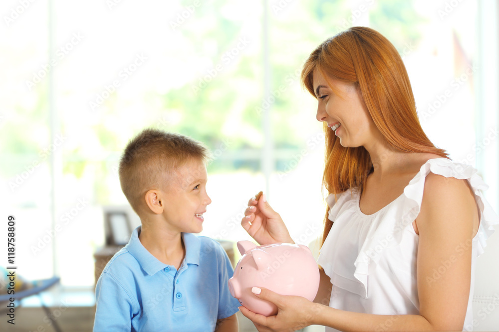 Savings concept. Mother and little boy putting coins into piggy bank Savings concept. Mother and little boy putting coins into piggy bank