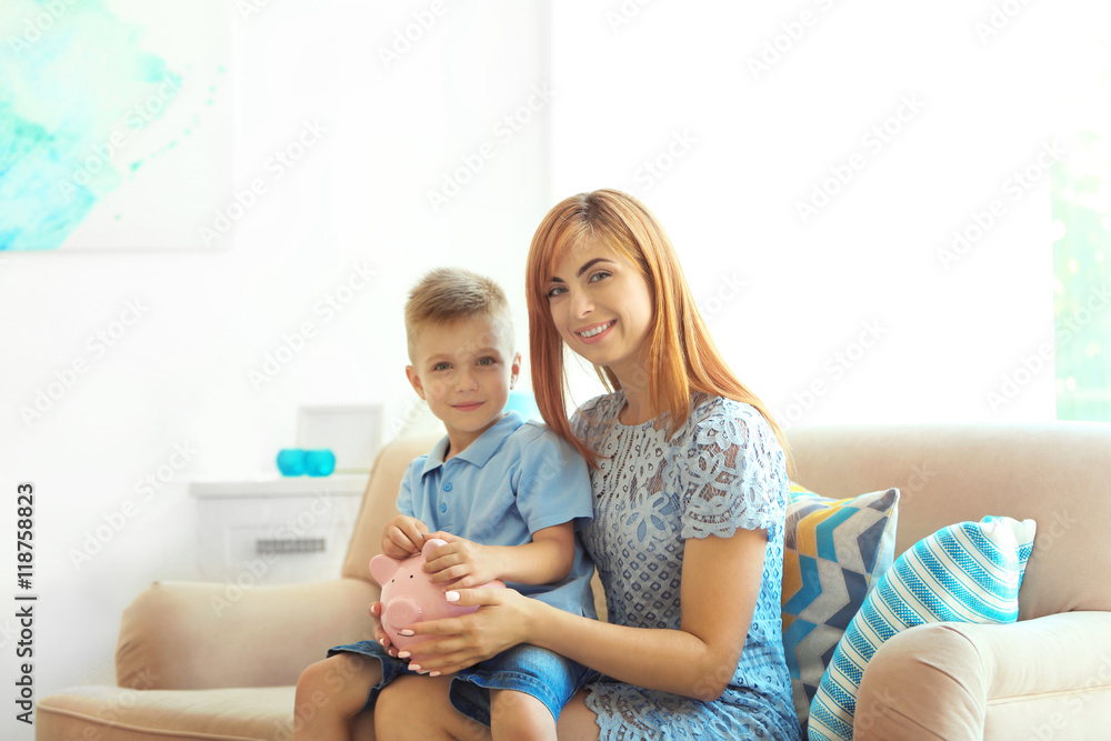 Savings concept. Mother and little boy sitting on sofa with piggy bank Savings concept. Mother and little boy sitting on sofa with piggy bank
