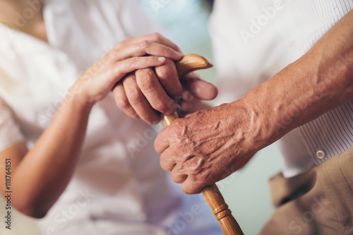 Young woman holding hand of old man with walking stick