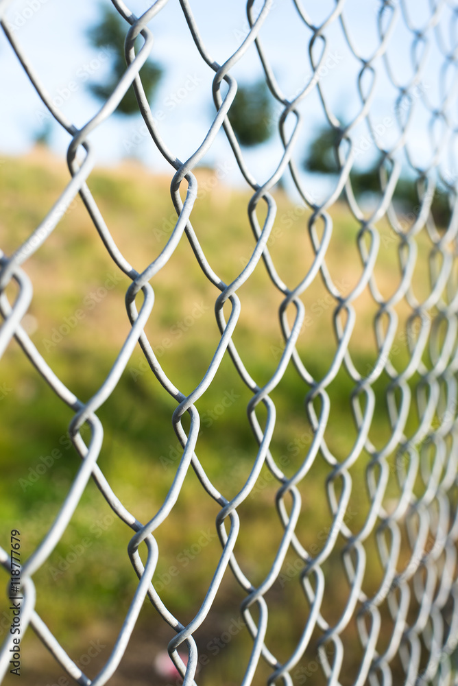 metal fence in a green field, trees behind the fences, closeup, horizontal metal fence in a green field, trees behind the fences, closeup, horizontal