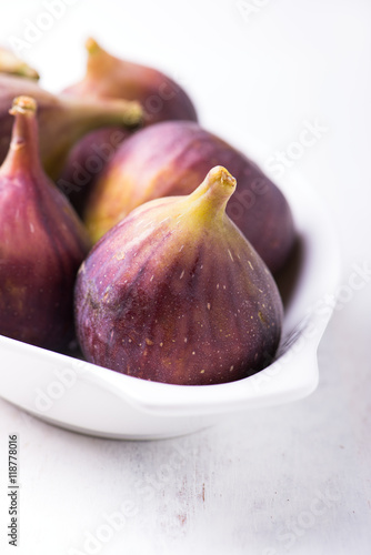 close up of organic, fresh figs in a white dish and isolated on rustic white wooden board, vertical with copy space