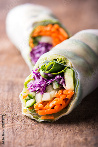 close up of fresh and vegan rice paper spring rolls with raw vegetables (cucumber, avocado, lettuce, carrots, red cabbage) inside, isolated over dark, wooden background