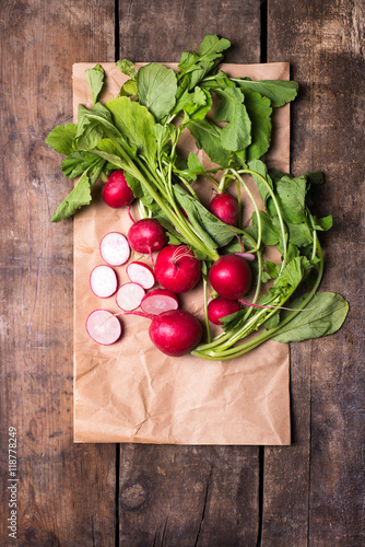bundle of organically grown, freshly harvested, red radishes with cuts on a recycled paper, isolated over rustic wooden background, close up, top view