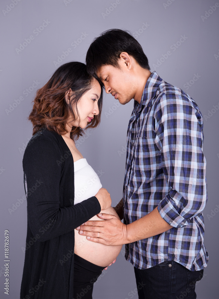 young couple: pregnant mother and happy father on gray backgroun young couple: pregnant mother and happy father on gray backgroun
