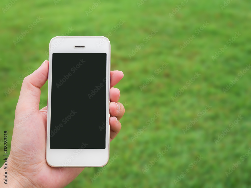 Human hand holding mobile phone against blurred green field background with copy space