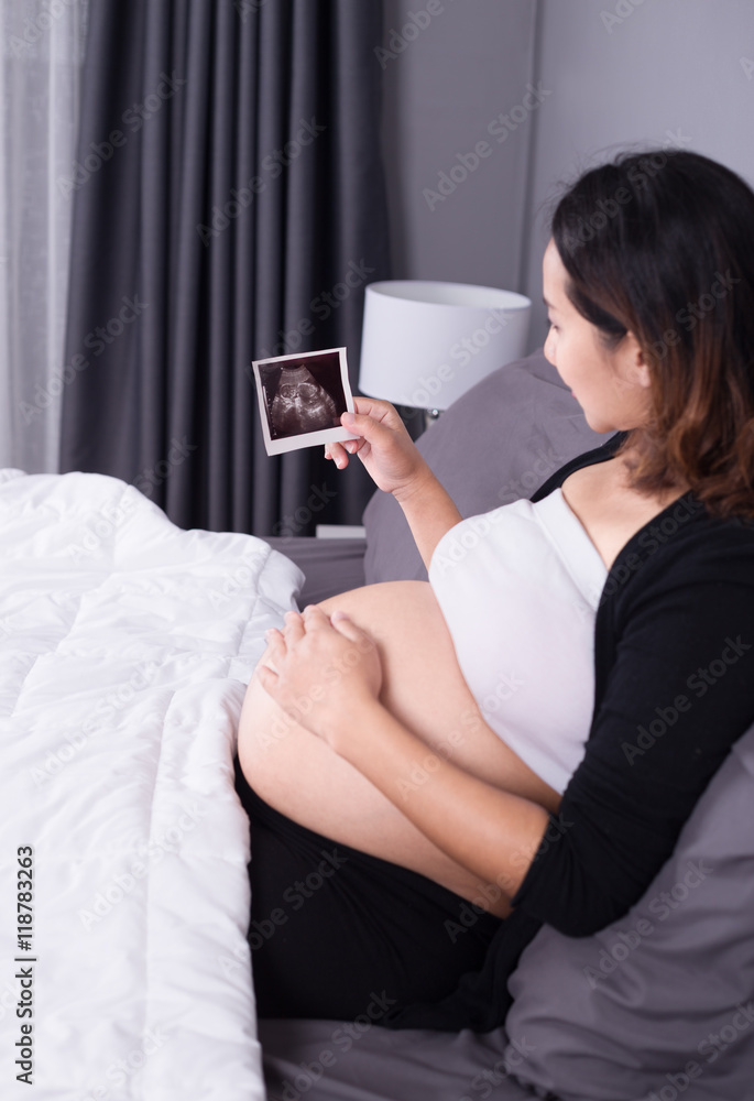 pregnant woman with ultrasound image of baby sitting on bed in b pregnant woman with ultrasound image of baby sitting on bed in b