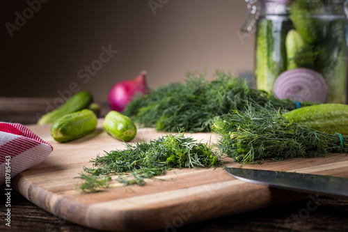 Sliced twig of dill on a wooden board with cucumber and jar