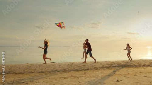 Happy and carefree childhood. Children playing with older kite, running across the sand, laughing photo