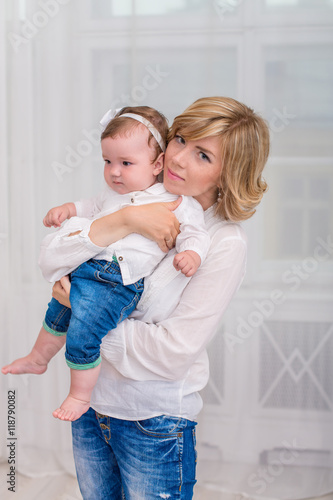 Happy mother holding a daughter in her arms. Mom and daughter dressed in white shirt and jeans