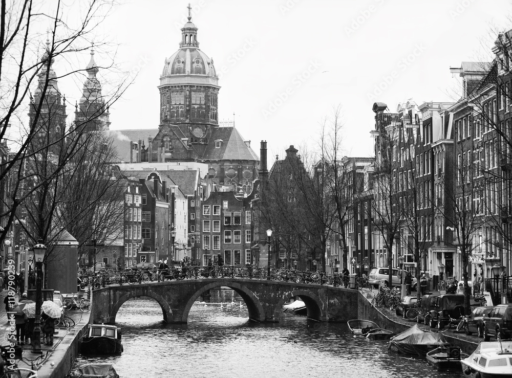 Naklejka premium The Oudezijds Voorburgwal a street and canal in the Red-light district in the center of Amsterdam. In the background Basilica of St. Nicholas. Black and white